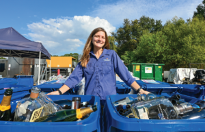 Cassidy poses infront of new Glass Recycling Canisters filled with glass.