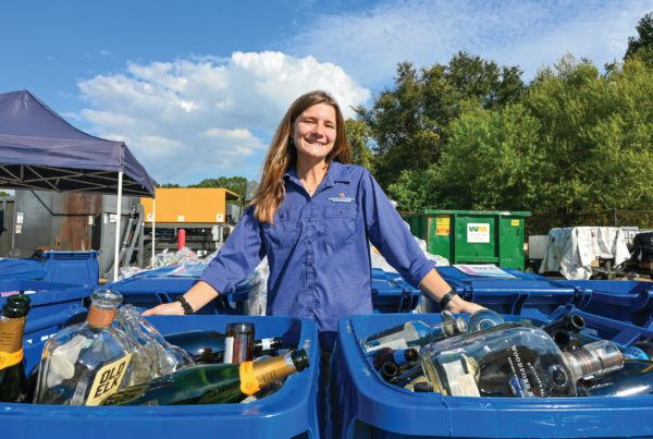 Cassidy poses infront of new Glass Recycling Canisters filled with glass.